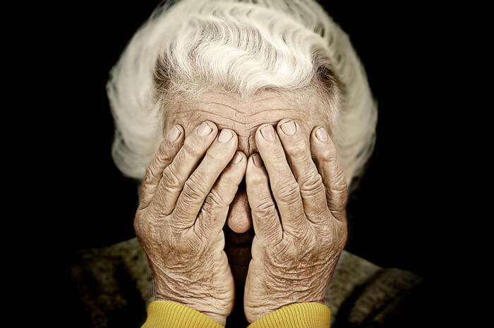 alte Frau mit Händen vor Gesicht