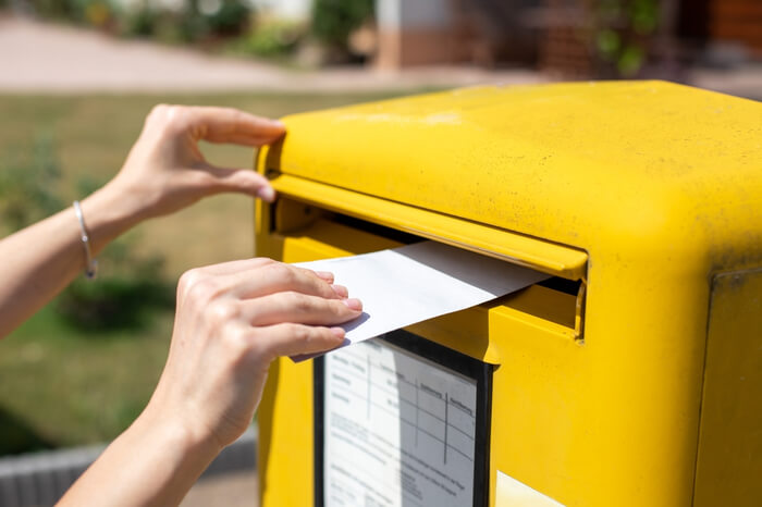Person steckt Brief in Briefkasten der Deutschen Post