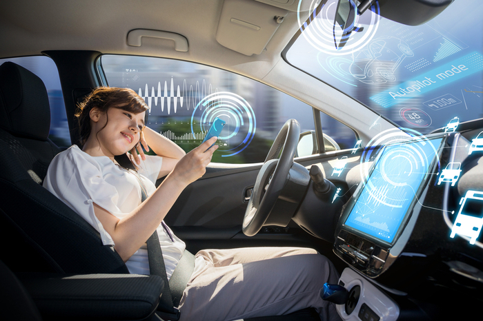 Cockpit eines autonomen Autos Frau auf Fahrersitz schaut auf Smarthpone