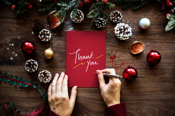  Person schreib auf weihnachtlichem Holztisch eine Dankeskarte